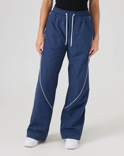 Model wearing Roxy Stevie Parachute Pants in Mood Indigo, featuring white piping, paired with a black top. Only the lower half is shown against a plain white background.