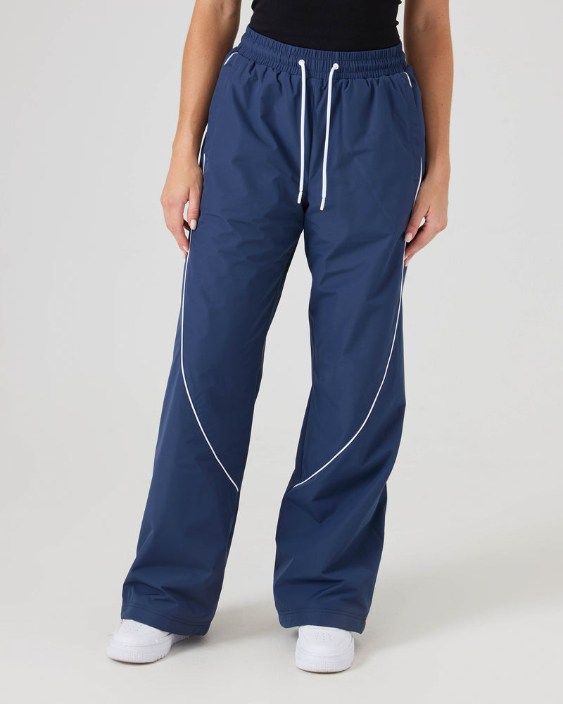 Model wearing Roxy Stevie Parachute Pants in Mood Indigo, featuring white piping, paired with a black top. Only the lower half is shown against a plain white background.
