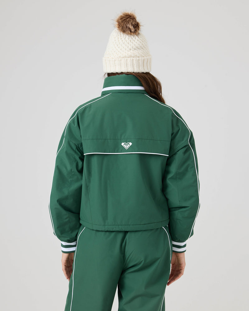 A person is seen from behind wearing a green Roxy Emily Track Jacket with white trim, relaxed fit, adjustable hem, and small logo, paired with a white knit beanie with pom-pom.