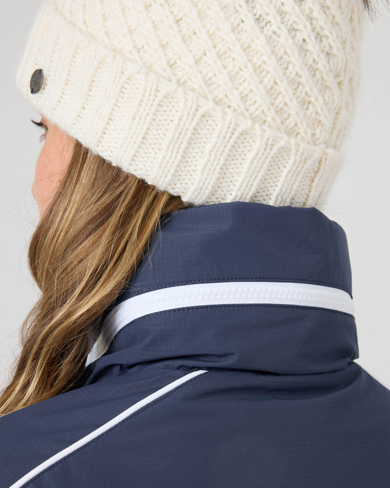 A person with long, wavy hair wears a white knit beanie and the Roxy Emily Track Jacket in navy with white trim, shown from the back and slightly to the side.
