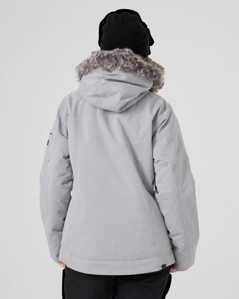 A person wearing the Roxy Meade Jacket—a light gray women’s snowboard jacket featuring a faux fur-lined hood—for insulated warmth, paired with a black beanie and photographed from the back against a plain white background.