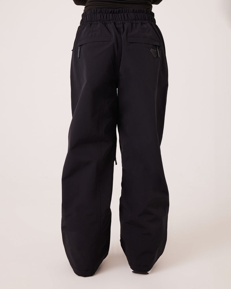 A person wears the Roxy Bleeker Pants—loose black trousers crafted from PFAS-free fabric, featuring an elastic waistband and zippered back pockets—while standing against a plain light background.