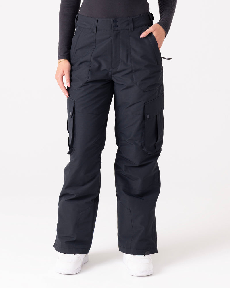 A person wearing Roxy Trooper Cargo Pants and a long-sleeve black top stands with one hand in a pocket against a plain white background.
