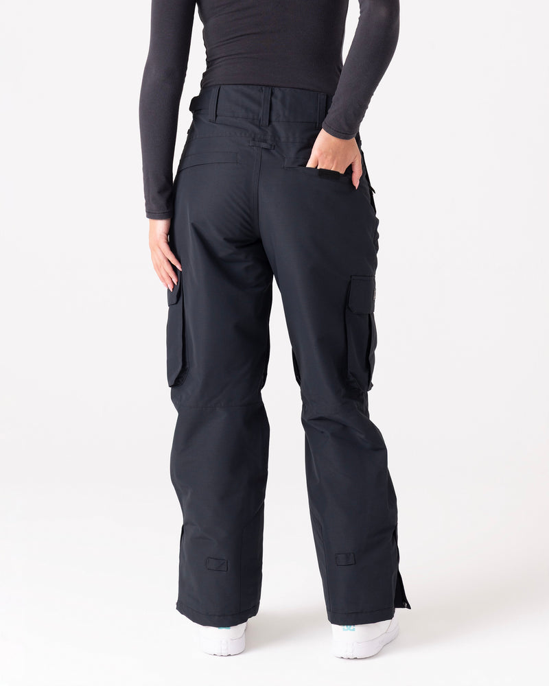 A person wearing Roxy Trooper Cargo Pants in black and a long-sleeve black top stands facing away, with one hand in a back pocket and white shoes visible.