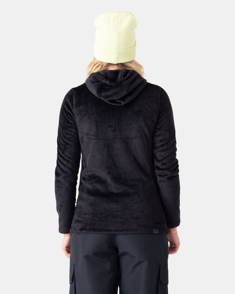 A person wearing a light yellow beanie, black Roxy Jetty 3N1 Jacket made from recycled materials, and black pants, stands with their back to the camera against a plain light background.