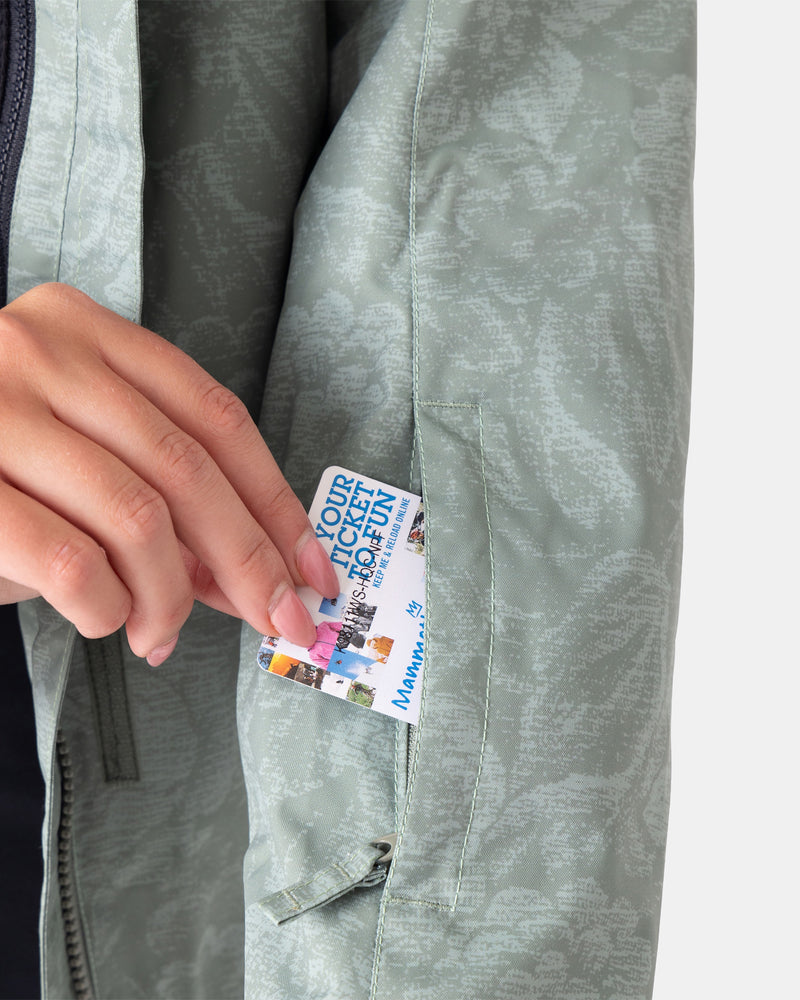 A hand places a colorful ticket into the zippered sleeve pocket of the light gray patterned Roxy Jetty 3N1 Jacket, crafted from recycled materials.