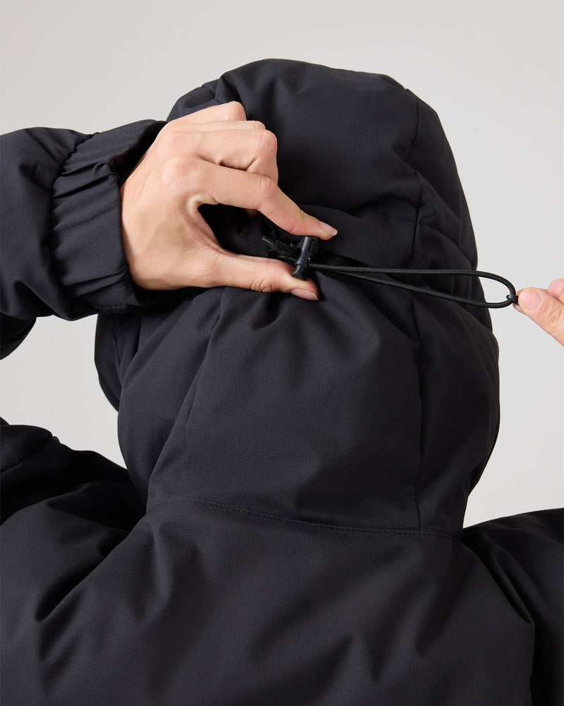 A person adjusts the drawstring on the hood of a black Roxy Jewelz Jacket, pulling the cord tight with their hand.