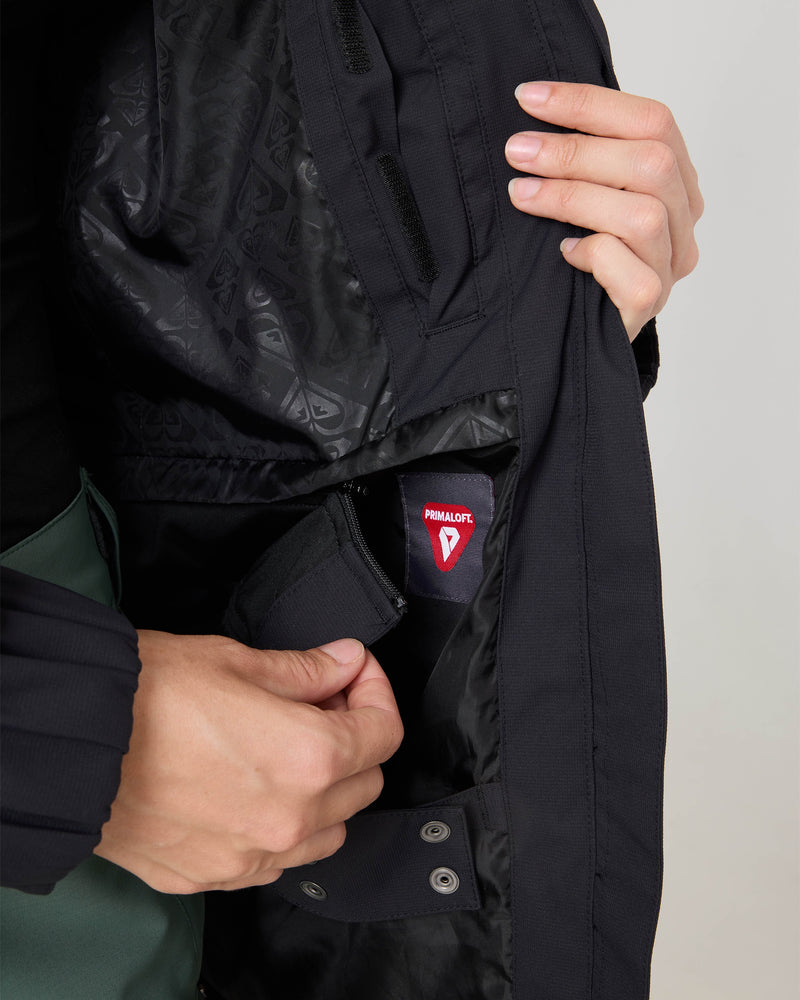 A person opens a black Roxy Jewelz Jacket to reveal a red PrimaLoft tag on the inner lining, highlighting the details of the jacket’s interior and fasteners.