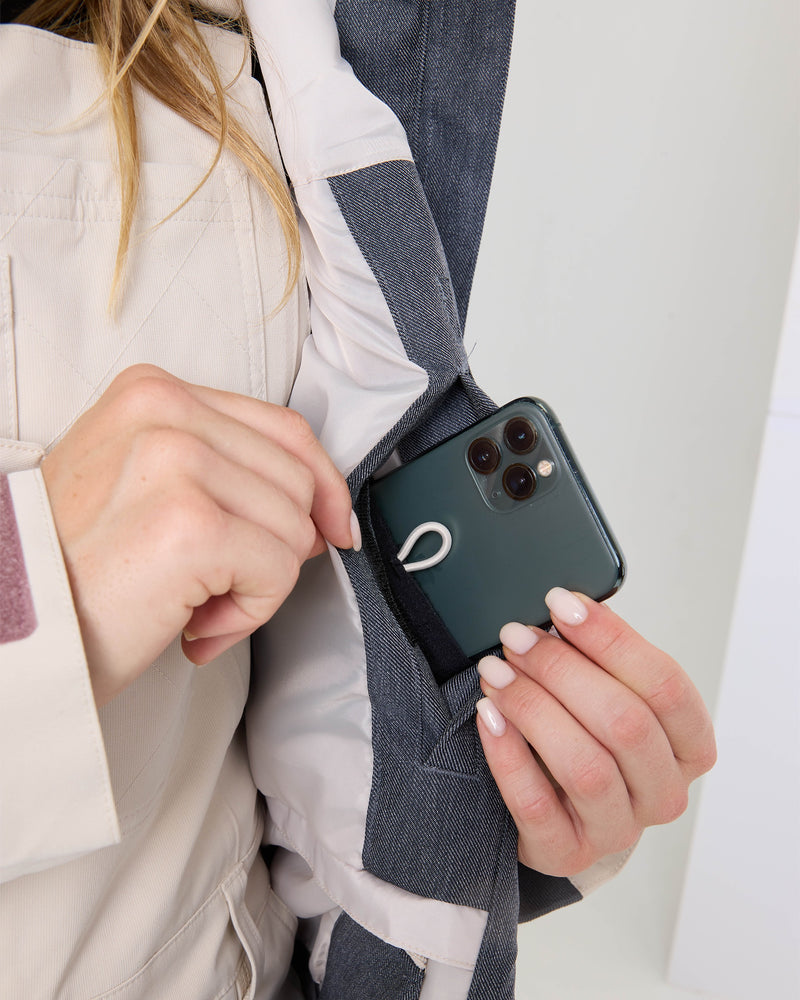 Wearing the Roxy Cheer Up Jacket—a technical outerwear piece in light and dark gray designed for staying organized on the go—a person slips a three-camera smartphone with a small white cord holder attached to the back into an inner pocket.