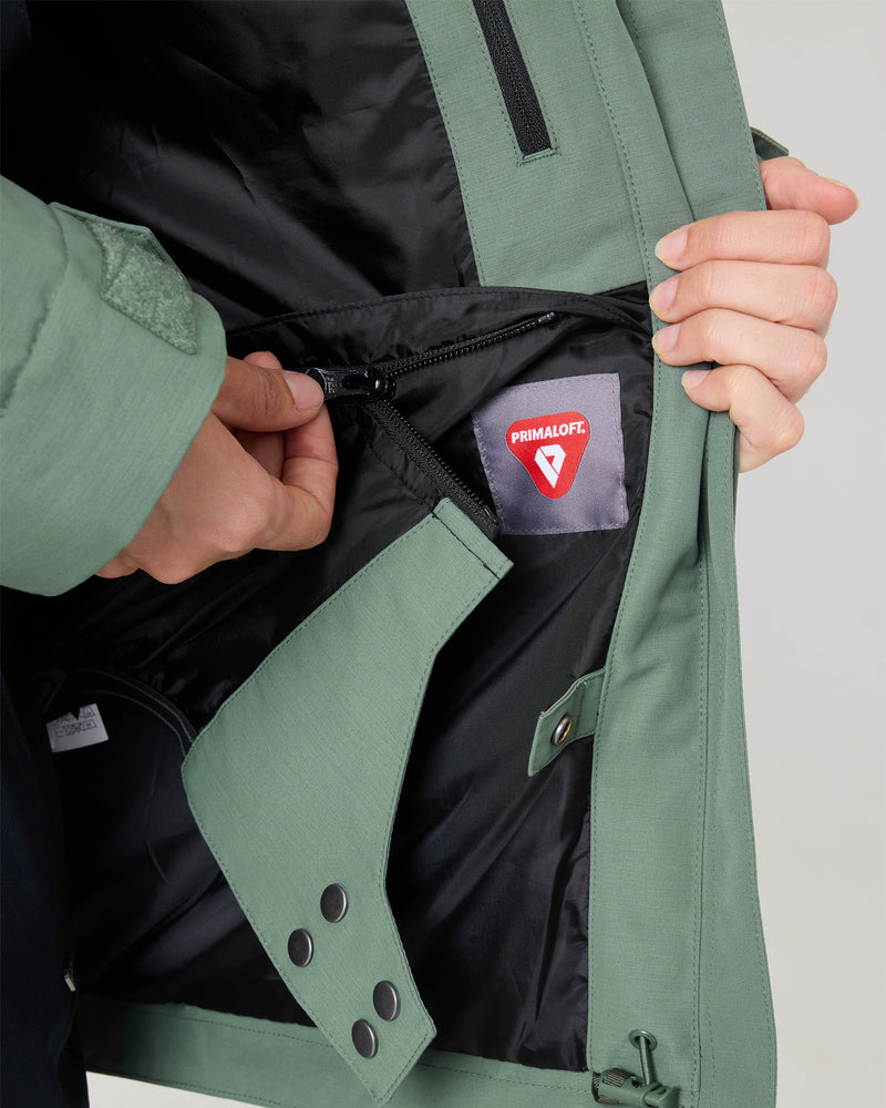 A person shows the inside of the green Roxy Free Love Jacket for women, highlighting a zippered pocket and a red Primaloft insulation tag sewn into the black lining.