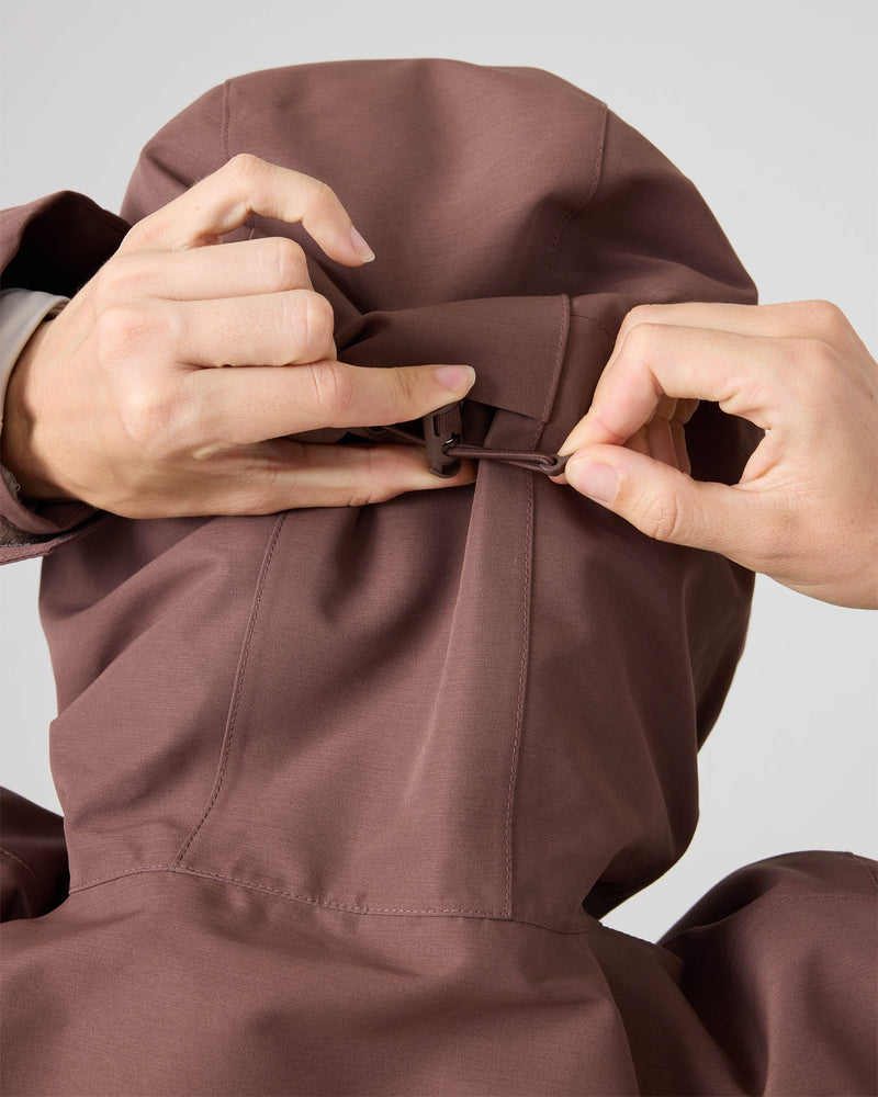 A woman adjusts the back hood drawstring on a brown Roxy Free Love Jacket with PrimaLoft insulation, shown from behind.