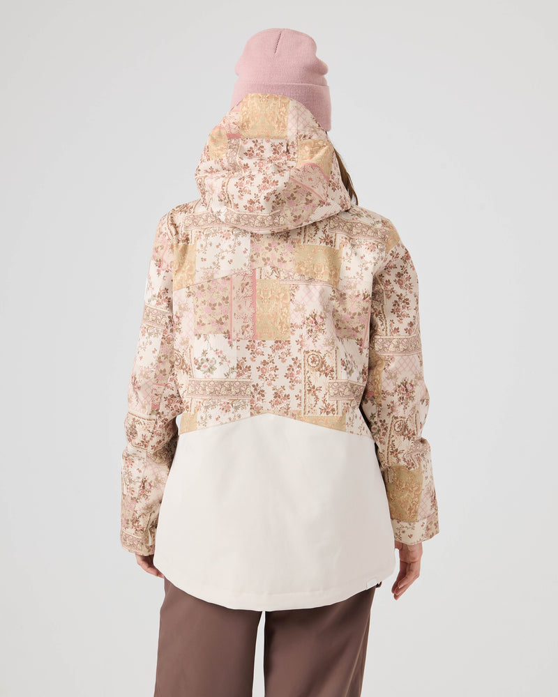 A person is seen from behind against a plain light background, wearing the Roxy Incline Jacket with a hood, paired with mauve pants and a pink beanie. This patterned women’s snow jacket delivers 15K protection, seamlessly combining style and functionality for winter conditions.