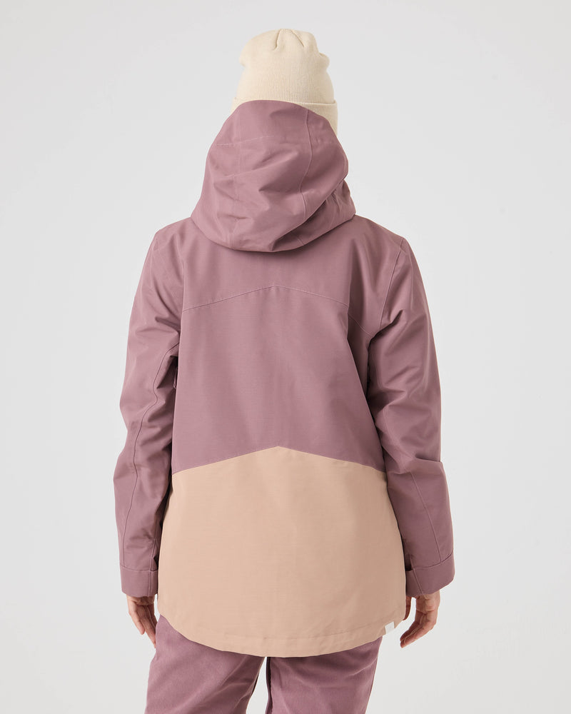 A person stands against a plain white background, shown from the back, wearing a light beige beanie and the Roxy Incline Jacket—a women’s snow jacket in two-tone mauve and beige with 15K protection.