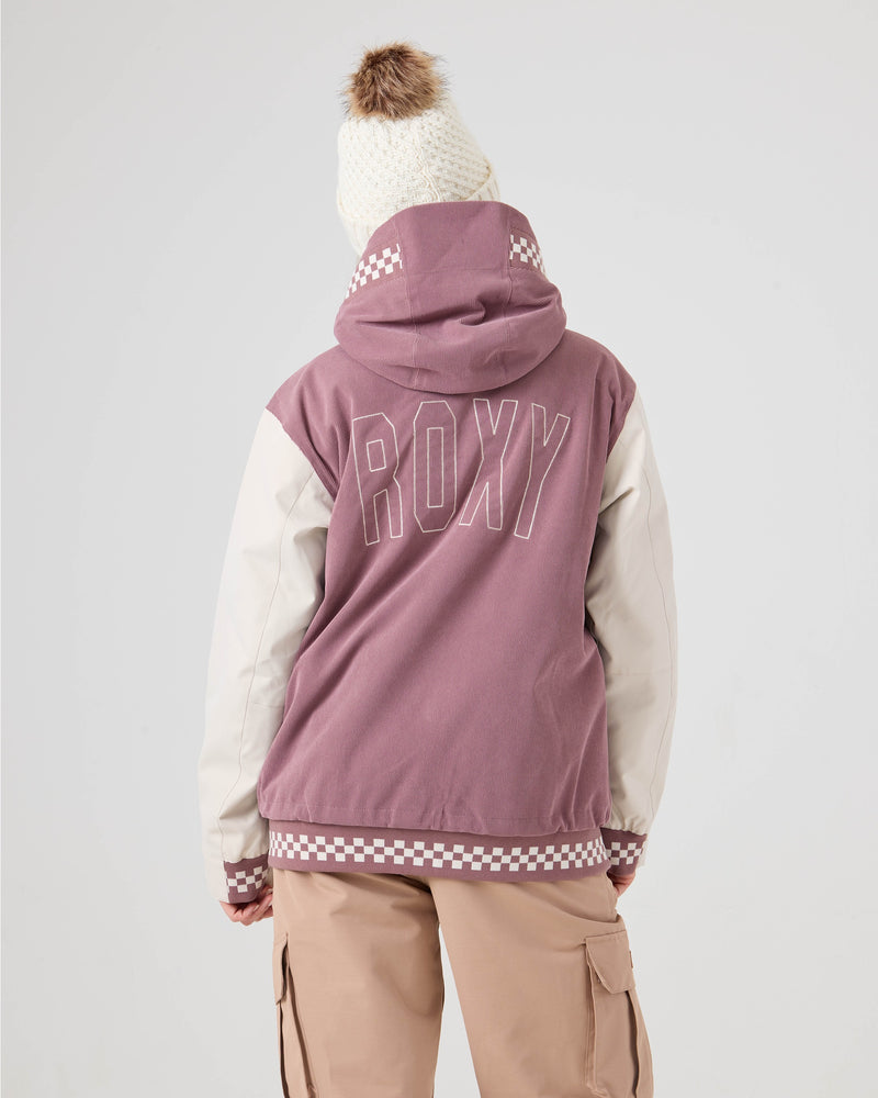 A person wearing the Roxy Cheer Up Jacket in pink and white, paired with beige cargo pants and a white knit beanie topped with a brown pom-pom, stands facing away from the camera against a plain light background.