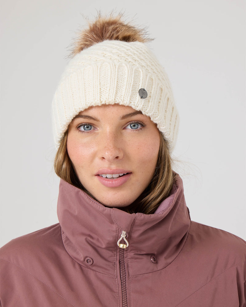 A woman wears a mauve Roxy Snowdrift Jacket, crafted from recycled polyester faux down, along with a white knit hat featuring a pom-pom. She faces forward with a neutral expression against a light background.