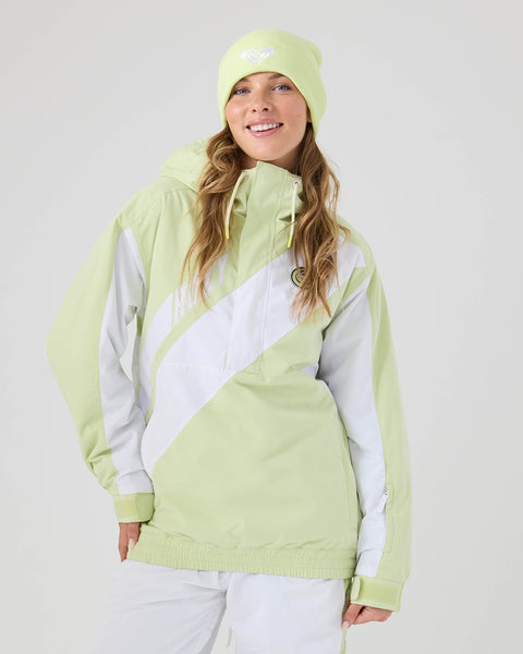 A woman smiles while wearing the Roxy Chloe Kim Majesty Anorak in Lily Green—a women’s snowboard jacket crafted from recycled fabric—paired with a matching beanie and white pants, set against a plain light background. This stylish Roxy jacket delivers comfort and weather protection for any winter adventure.