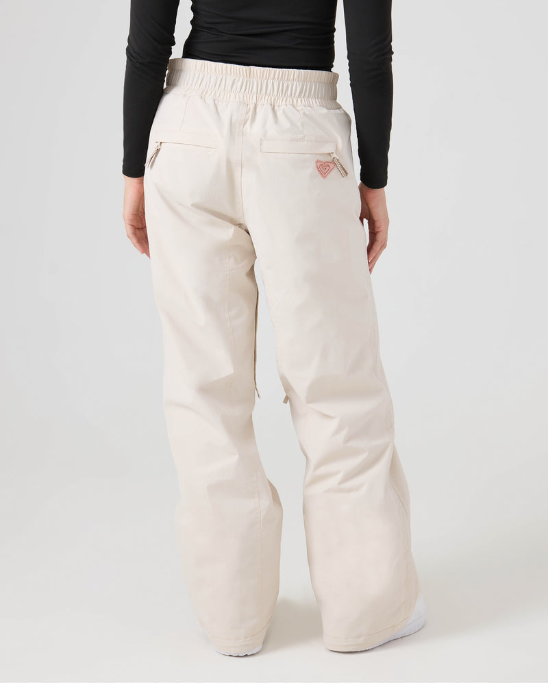 A person is shown from the back wearing off-white, loose-fitting Roxy Bleeker Pants and a black long-sleeve top against a plain light background. The women’s snow pants feature two back pockets, an elastic waistband, and provide 10K/5K protection for reliable performance in varying conditions.
