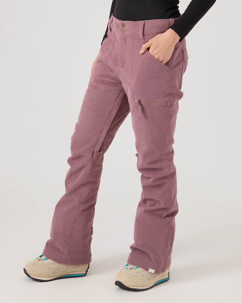 A person stands with hands in the side pockets of the tailored-fit Nadia Pants by Roxy in mauve corduroy, paired with beige shoes and facing slightly to the side against a plain background.