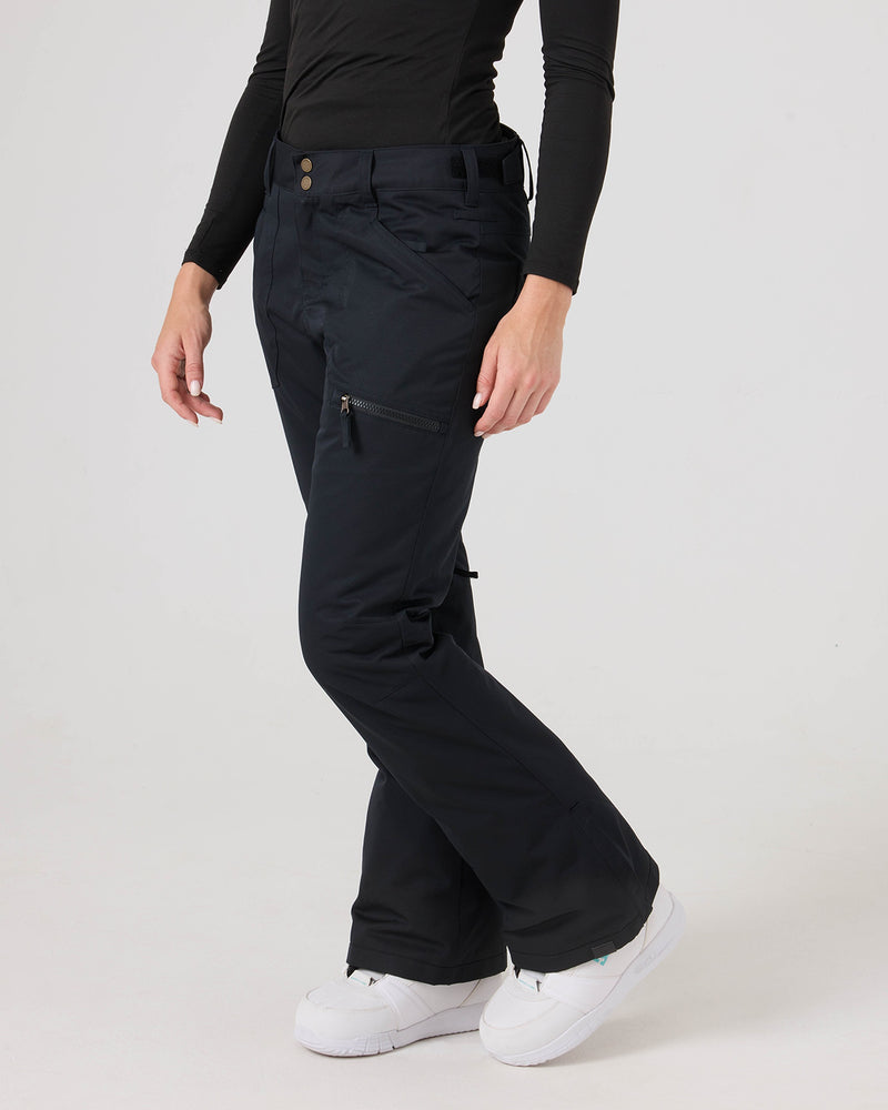 A person wearing Roxy Nadia Pants in black—crafted from waterproof corduroy fabric—paired with a fitted long-sleeve black top and white sneakers stands against a plain white background. Their face is not visible in the image.
