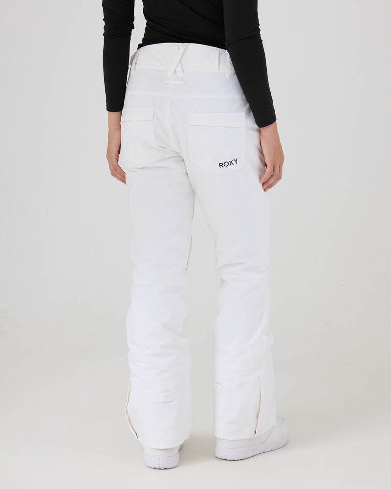 A person stands facing away, wearing the Roxy Backyard Pants in white—women’s snow pants made from recycled polyester with 10K/5K protection. The pants feature back pockets, one of which displays ROXY branding, and are paired with a black long-sleeve top. The background is plain white.
