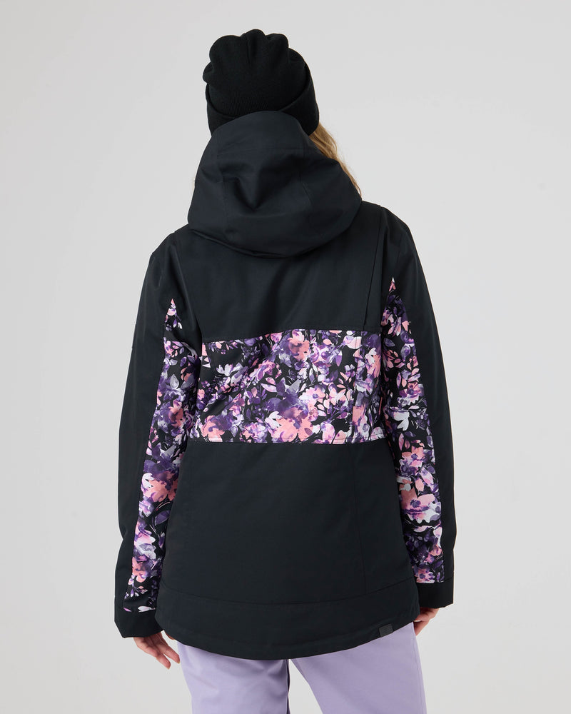 A person wearing a black beanie and the Roxy Presence Parka Jacket—styled with a purple and pink floral pattern on the back and sleeves—stands facing away from the camera against a plain light background. This jacket delivers 15K/15K performance for both function and flair.