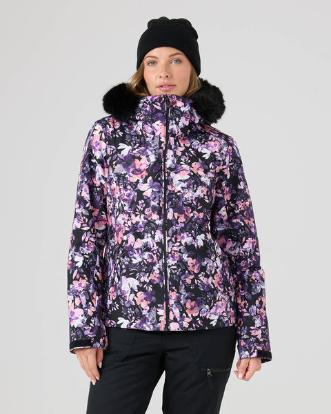 A woman wearing a black beanie and the Roxy Jet Ski Jacket in Blended Bouquet—a floral-patterned, waterproof, insulated jacket with a fur-trimmed hood—stands against a plain light background.