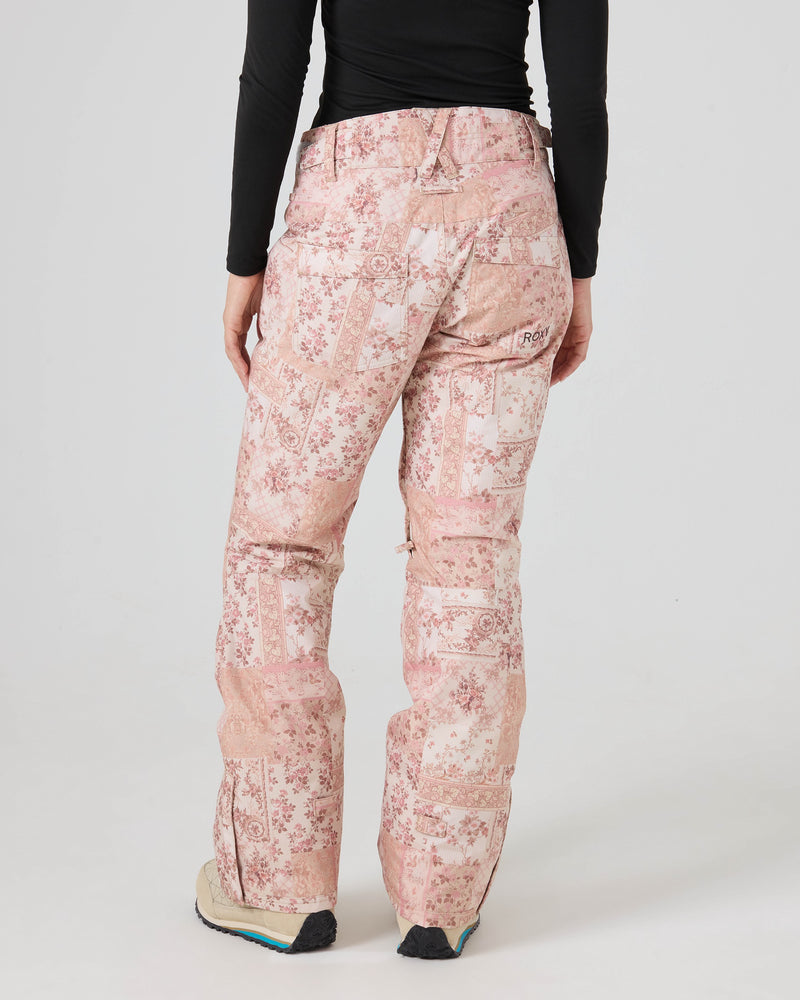 A person wearing Roxy Backyard Pants in a light pink pattern, paired with a black long-sleeve top and beige shoes, stands with their back to the camera against a plain white background.