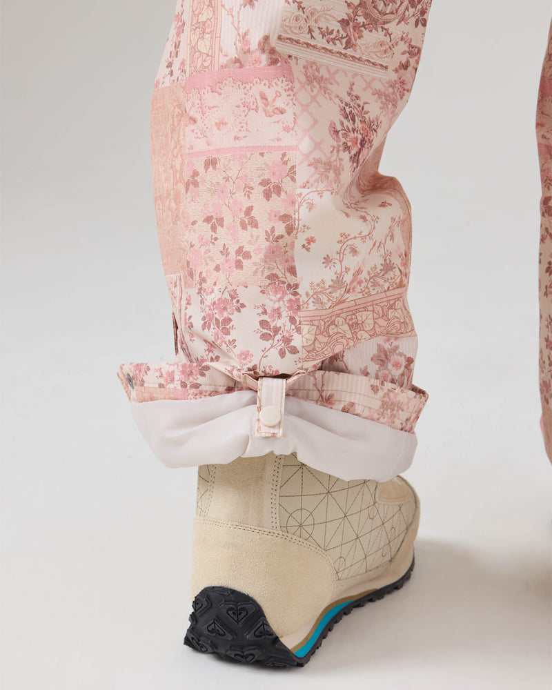 A close-up of a person’s lower leg in Roxy Backyard Pants, featuring a vibrant pink pattern and cuffed at the ankle, reveals a beige boot with a black sole and geometric designs. Crafted from recycled fabric that offers waterproof protection, these women’s snowboard pants stand out against the plain, light-colored background.