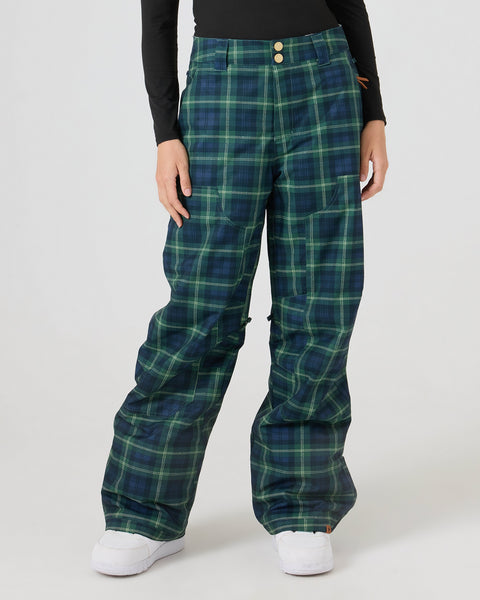 A person wearing Roxy Calico Pants in Tarten Plaid, paired with white shoes and a long-sleeve black top. The pants are made from recycled polyester. The image is cropped at the shoulders against a plain light background.