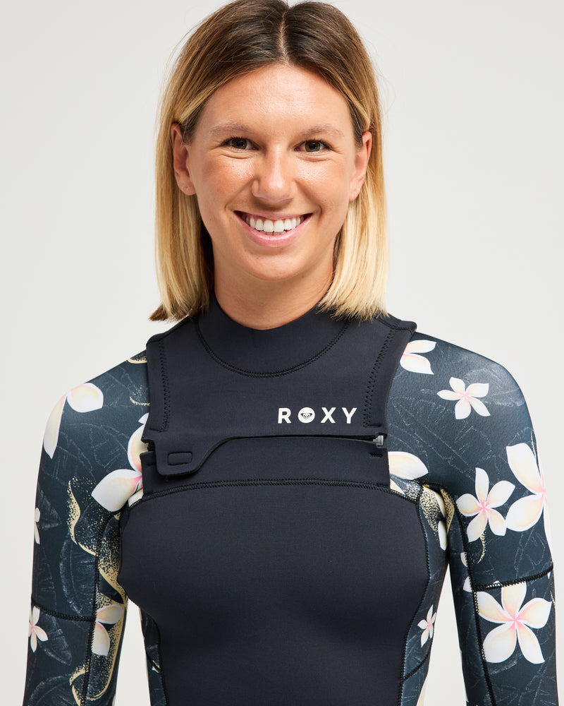 A smiling person with shoulder-length blonde hair wears the 4/3mm Swell Natural Front Zip Wetsuit by Roxy, standing against a plain light background.