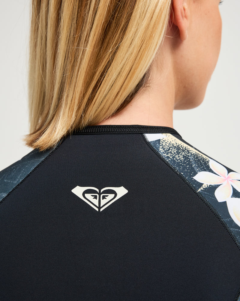 Woman with straight blonde hair wearing the Roxy 2mm Swell Natural Back Zip Spring Suit Wetsuit, visible from behind and slightly to the side.