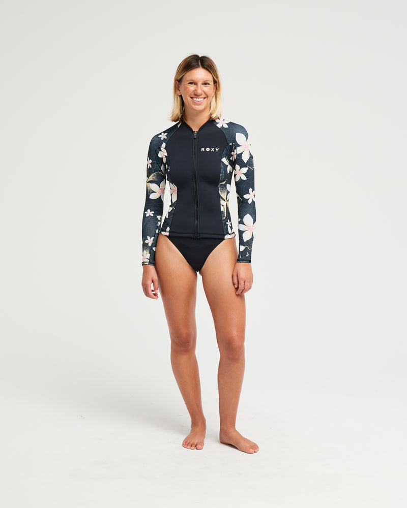 A person stands barefoot in the Roxy 2mm Swell Natural Back Zip Spring Suit Wetsuit in Hibiscus Real against a plain white background.