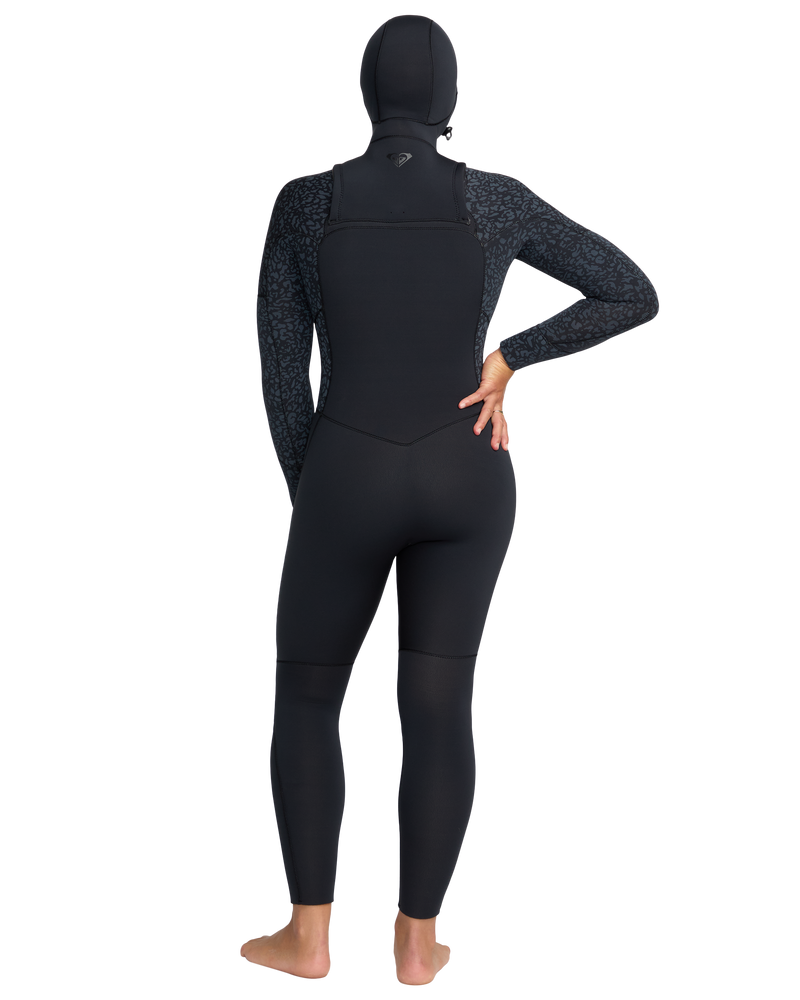 A person stands barefoot facing away, wearing the Roxy 5/4mm Swell Natural Hooded Front Zip Wetsuit with patterned sleeves, one hand on their hip, against a plain white background.