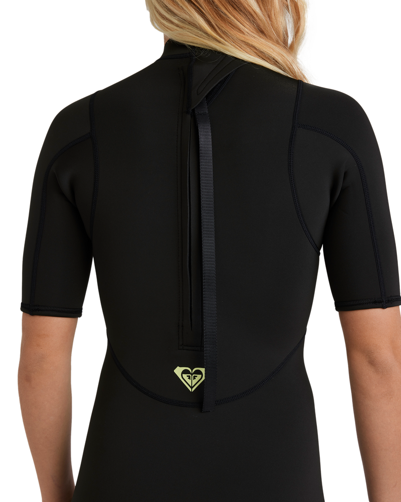 A person is seen from the back wearing the Roxy 2/2mm Prologue Short Sleeve (Flatlock) Wetsuit in black, which features a zipper with a pull strap and a small yellow logo near the lower back.
