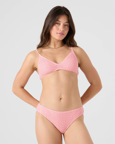 A woman with long brown hair and a subtle smile stands against a light background, wearing the Roxy Crochet Hipster Full Bikini Bottom. The bikini features thin straps and she poses with her hands on her hips.