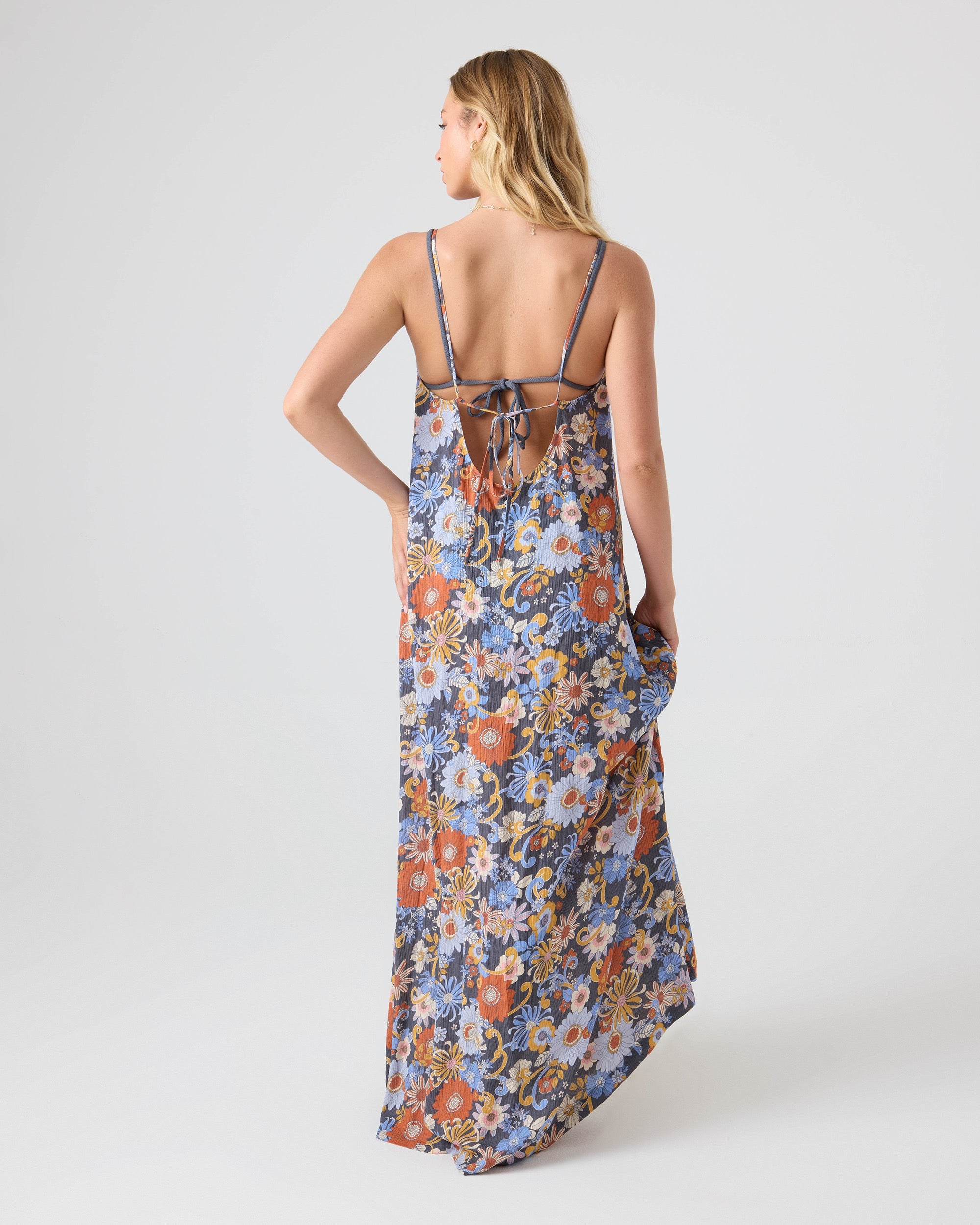 A woman faces away in the Roxy Soul Flower Cover Dress, a sleeveless tie-back maxi with an open back and thin center-tied straps. This chic floral beach cover-up features a colorful daisy and flower print.