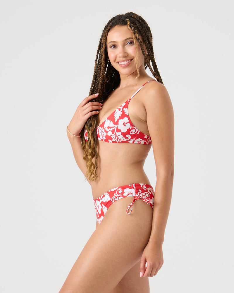 A woman with long braided hair smiles at the camera, wearing the Roxy Days Of Summer Athletic Triangle Bikini Top in a red and white floral print against a plain light background.