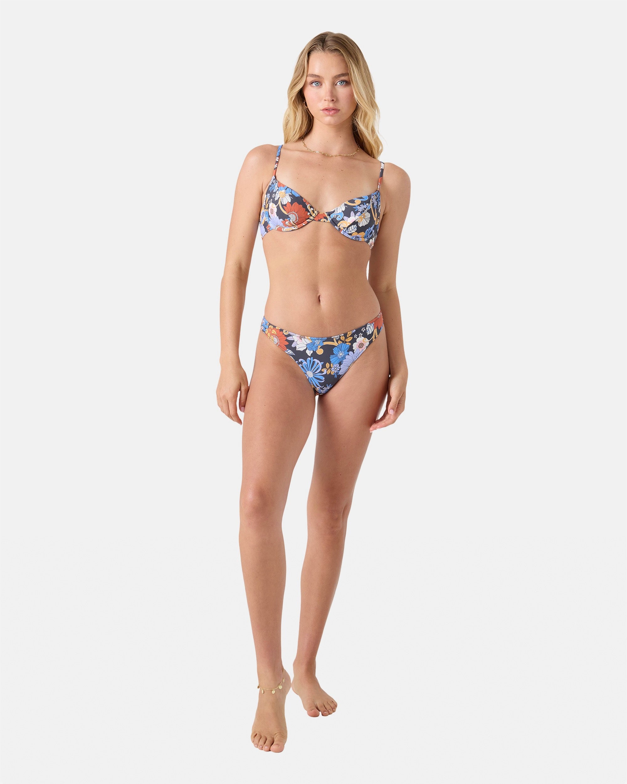 A woman barefoot and neutral-faced poses against a white background wearing the Roxy Soul Flower Smocked Demi Underwire Bikini Top in Gray Combo with matching recycled nylon bottoms, looking directly at the camera.