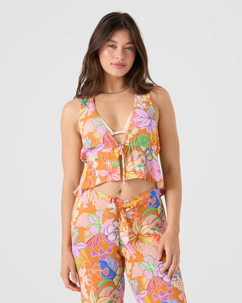 A woman wearing the Roxy Lei It On Me Cover Up Top, a colorful floral cropped tie-front design, and matching high-waisted pants stands against a plain light background, smiling slightly.