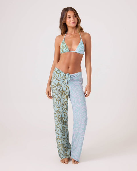 A woman poses barefoot in a blue and green leaf-patterned bikini top and matching Roxy Sea Bloom Front Tie Pant with an elastic waist, set against a plain background for a chic beach-ready look.