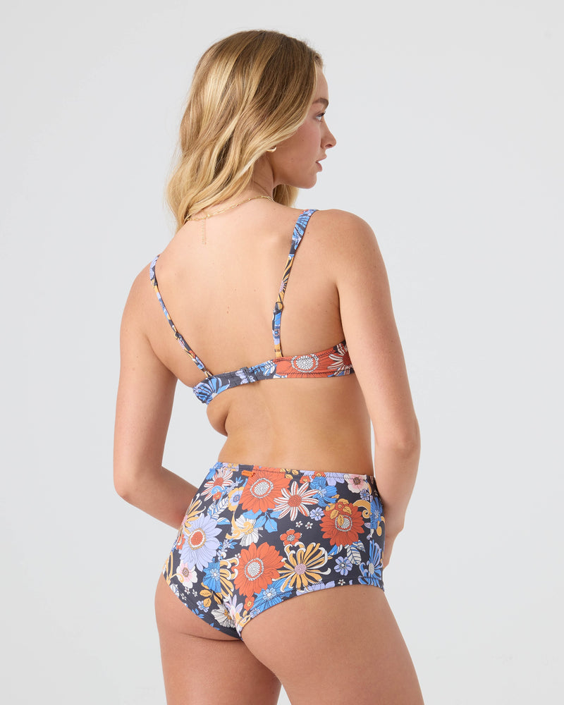 A woman with long blonde hair, seen from behind, wears the Roxy Soul Flower Scoop Bralette Bikini Top—a high-waisted blue, orange, and white floral swimsuit with adjustable straps—against a plain light background.