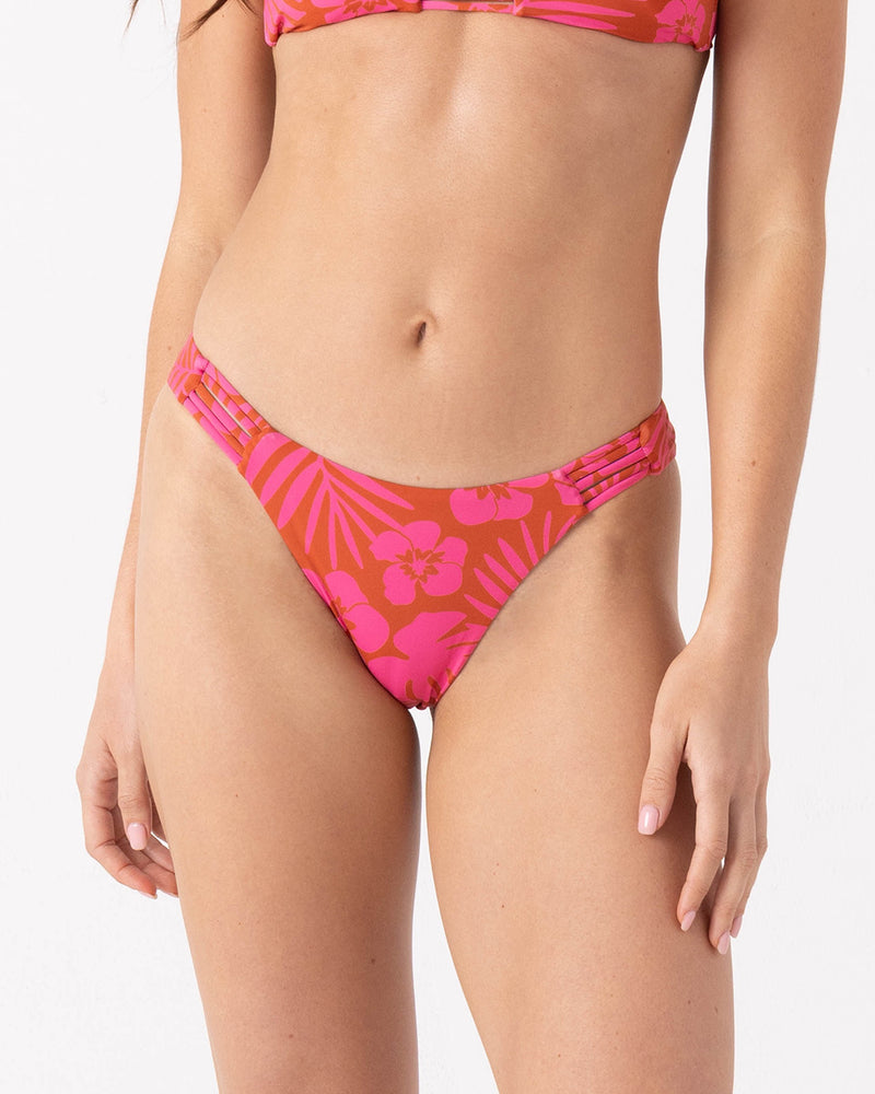 A woman wears the Roxy Sun Chasers Lattice Scoop Moderate Bikini Bottom in Pink Combo, featuring a high-leg cut, side cutouts, and pull-on fit, shown from mid-torso to upper thighs against a plain white background.