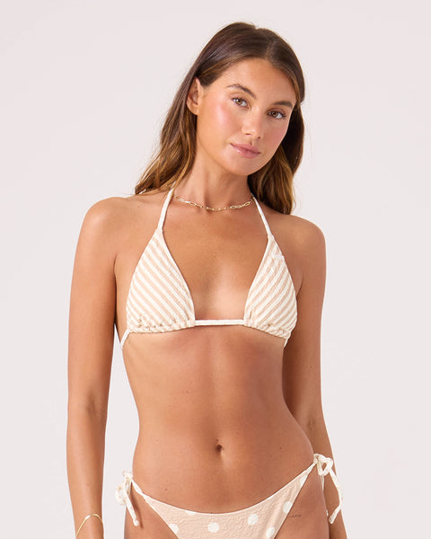 A woman wears the Roxy Polka Dots Mini Tiki Triangle Bikini Top in Neutral Combo, paired with matching bottoms, standing against a plain light background and gazing at the camera—ideal for a relaxed beach day.