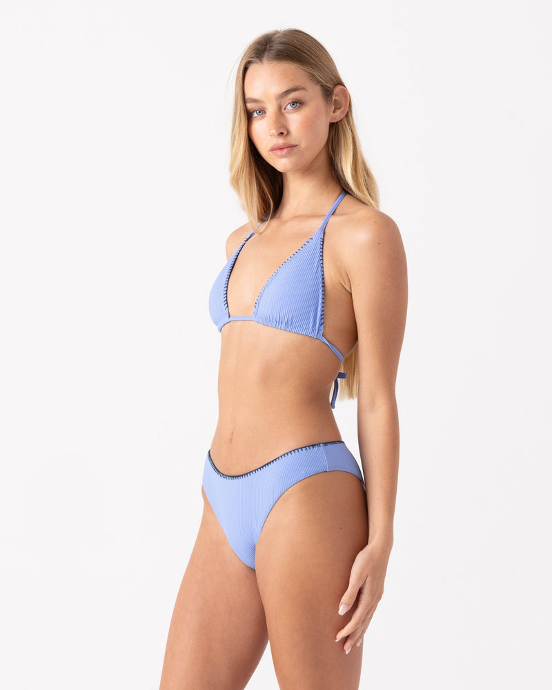 A woman with long blonde hair models the Roxy Loop Me In Scoop Cheeky Bikini Bottom in light blue, featuring a high-leg cheeky cut, against a plain white background, looking confidently at the camera.