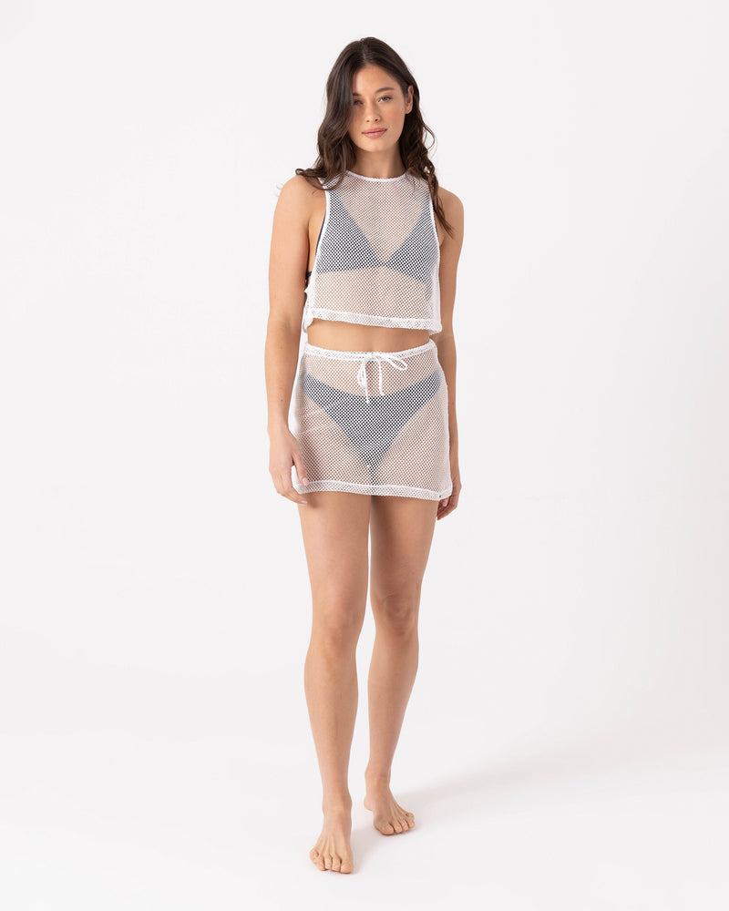 A woman stands barefoot against a white background, wearing the Roxy Don't Mesh With Me Crop Top Cover Up—a sleeveless, relaxed-fit top with a matching mesh skirt over a blue bikini. She faces forward with a neutral expression.