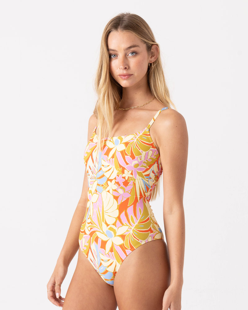 A woman models the Roxy Tropicool Low Back One Piece Swimsuit in vibrant floral print, made from buttery-soft fabric, standing against a plain white background and looking calmly at the camera.
