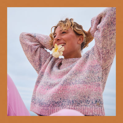 Woman wearing a pink sweater with a flower in her hair against a blue sky.