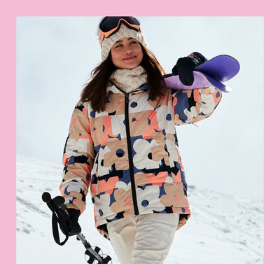 Person in a colorful jacket holding a snowboard in a snowy landscape