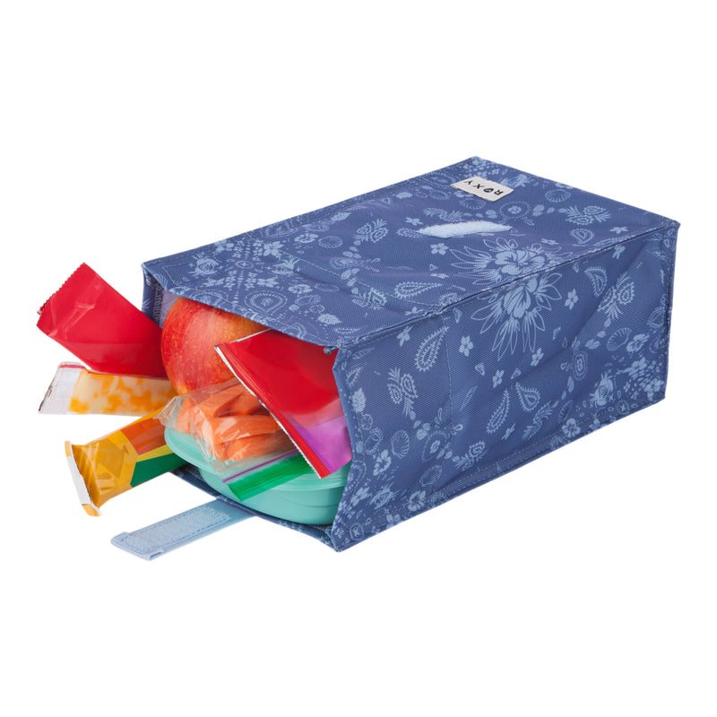 A Roxy Lunch Hour Lunch Bag in a blue floral design lies on its side with snacks, an apple, carrot sticks, and a container partially spilling out.