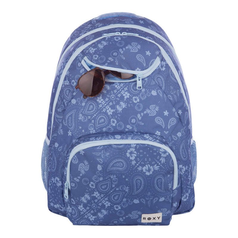 The Roxy Shadow Swell Backpack features a blue patterned design with white zippers and a prominent ROXY label. Brown sunglasses are tucked into the top front pocket, while multiple compartments and side mesh pockets offer versatile storage options.